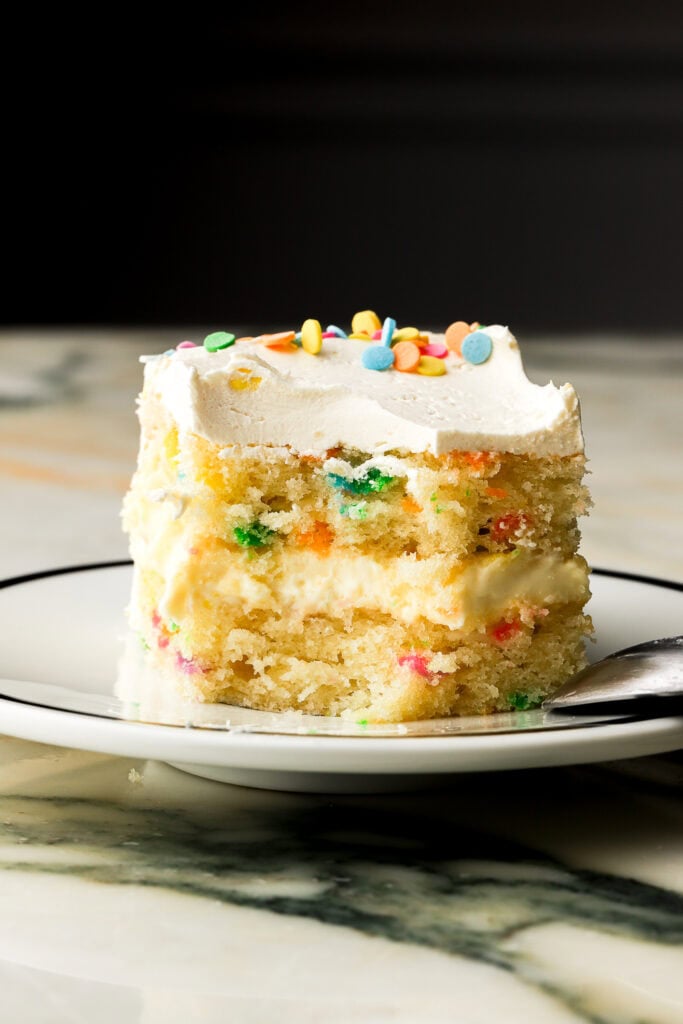 single layer of birthday cake on a plate with a bite missing, black background