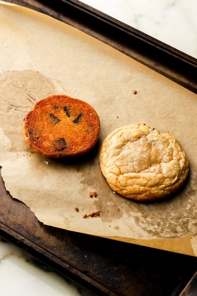 2 chocolate chip cookies on a pan, one flipped over to show the bottom. 