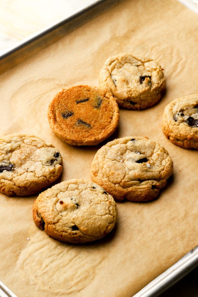 6 chocolate chip cookies on a pan, one flipped over to show the bottom. 