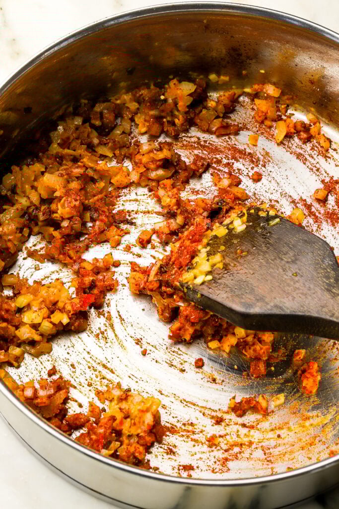flour and spices mixed into the veggies in a pan with a wooden spoon