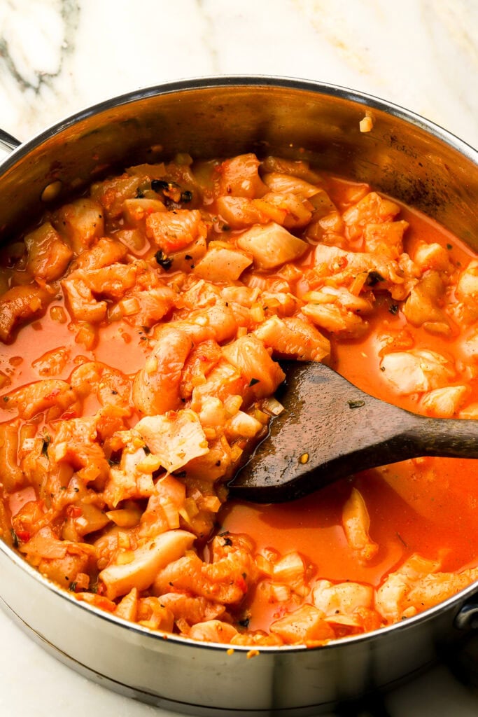 chicken and chicken broth cooking in pan with wooden spoon