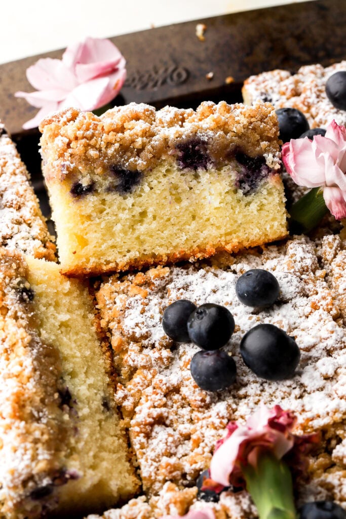 close up of a slice of blueberry coffee cake sitting up halfway on another one topped with blueberries