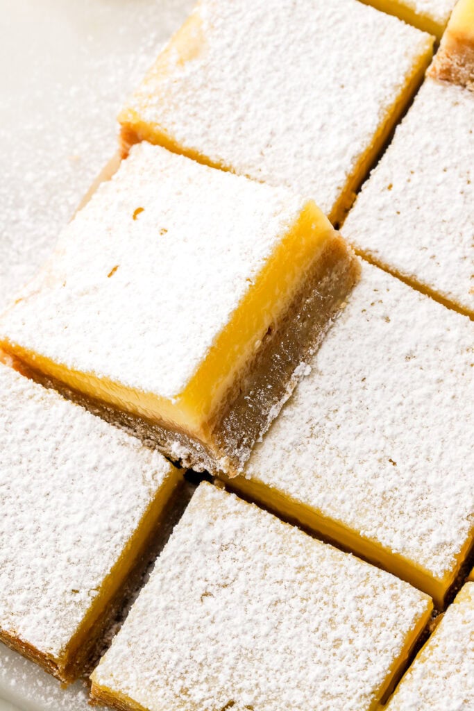 lemon bars dusted with powdered sugar and sliced, one sitting up higher on top of the others ones to show the inside texture