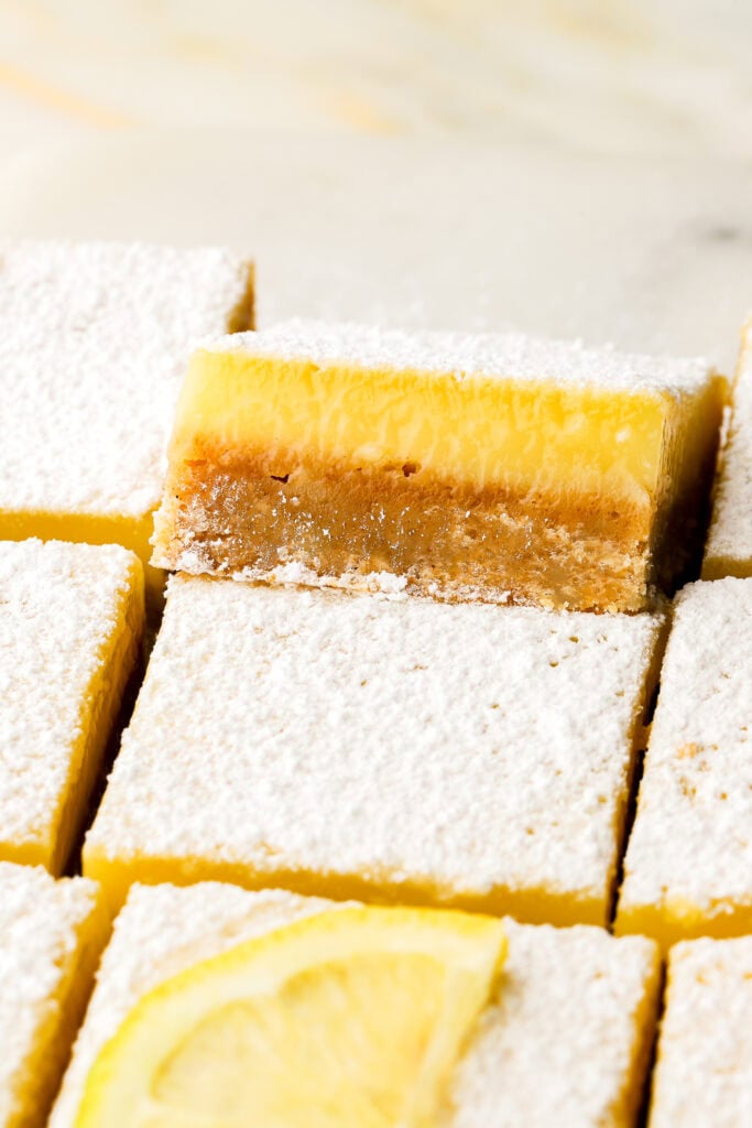 lemon bars dusted with powdered sugar and sliced, one sitting up higher on top of the others ones to show the inside texture