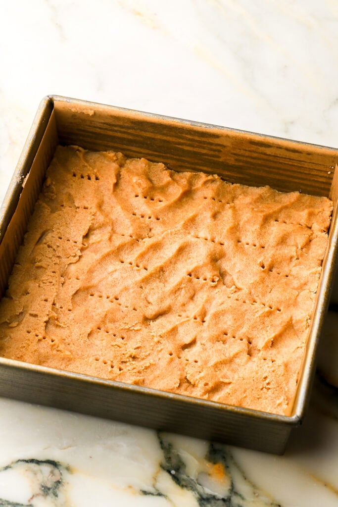 shortbread pressed into pan lined with parchment paper and fork holes poked into it.