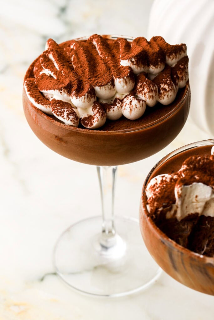 homemade chocolate mousse in a coupe glass topped with whipped cream and a dusting of cocoa powder