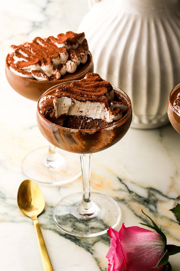 two coupe glasses filled with chocolate mousse and whipped cream with a bite taken out of one