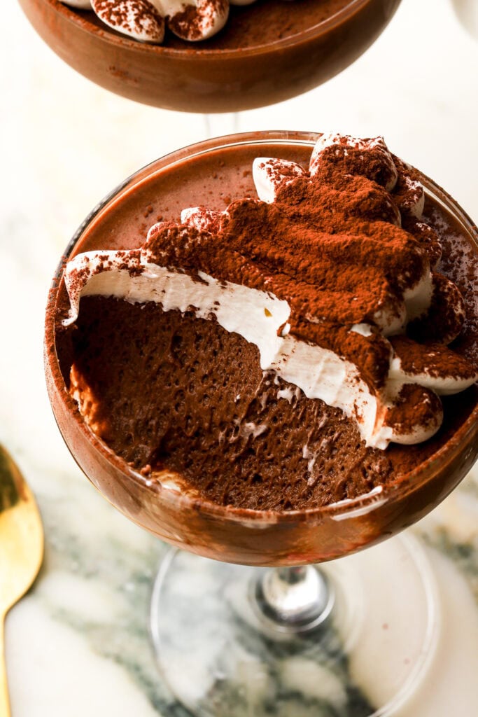 close up of chocolate mousse with whipped cream in a coupe glass with a bite taken out to show the texture