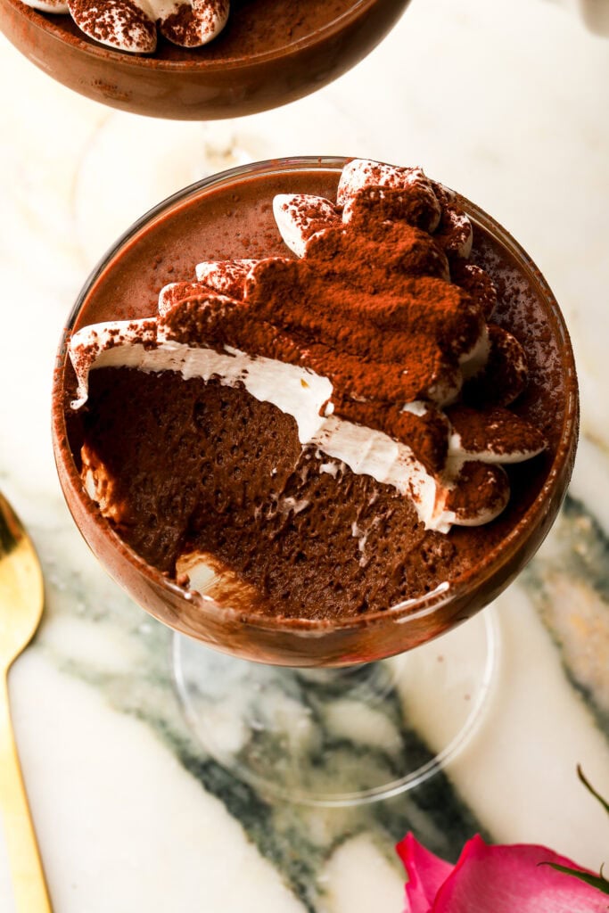 close up of chocolate mousse with whipped cream in a coupe glass with a bite taken out to show the texture