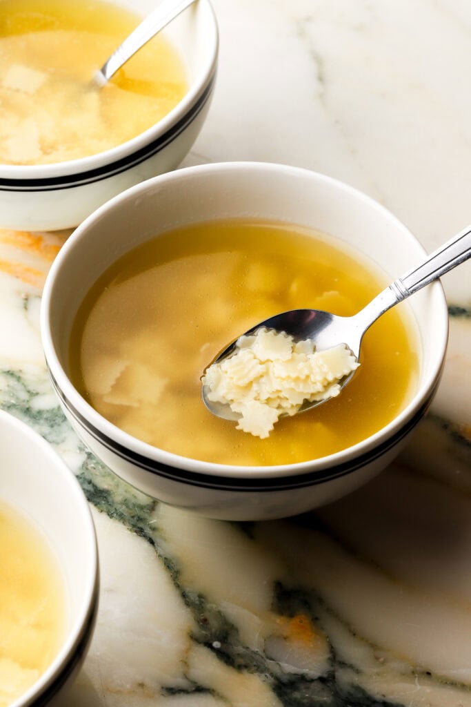 three bowls of chicken soup with square noodles on a marble counter top.