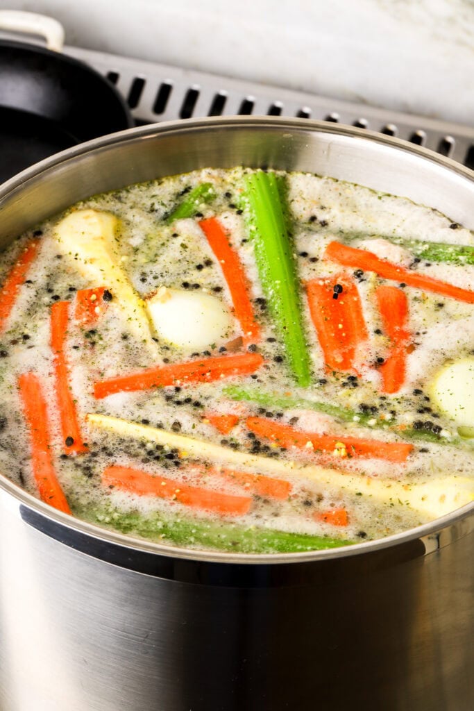 foam collecting on top of soup in a large pot, vegetables rising