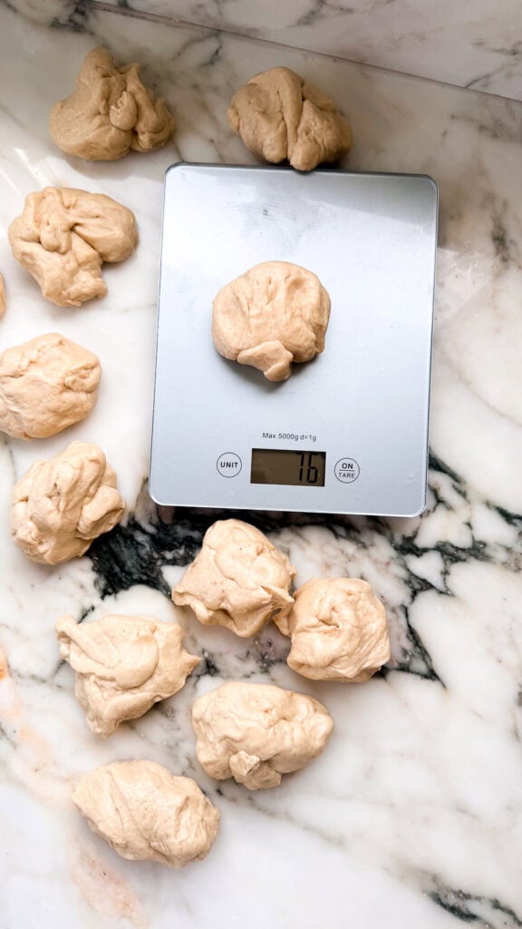balls of dough getting weighed on a kitchen scale for even sizing