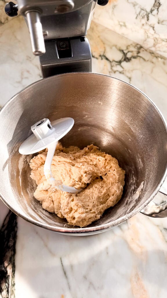 dough before butter is added in a stand mixer bowl with the hook attachment
