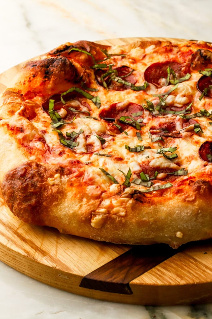 finished pizza - hand stretched; on a cutting board and topped with fresh chopped basil