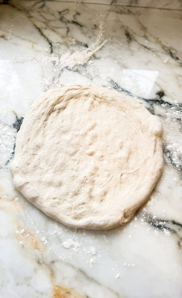 pizza dough hand stretched on floured surface