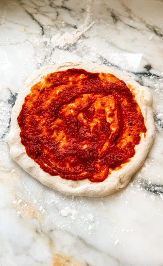 hand stretched pizza topped with pizza sauce