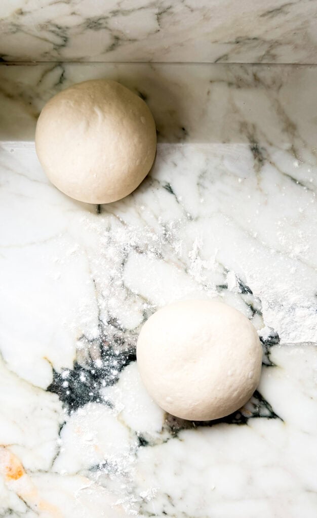 two pizza dough balls proofing on the counter