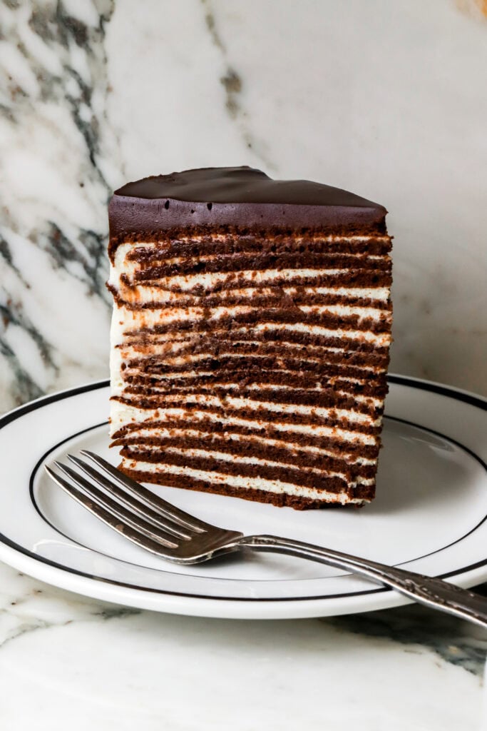 slice of cake standing up with 16 chocolate cake layers and vanilla cream - on a white plate with a fork