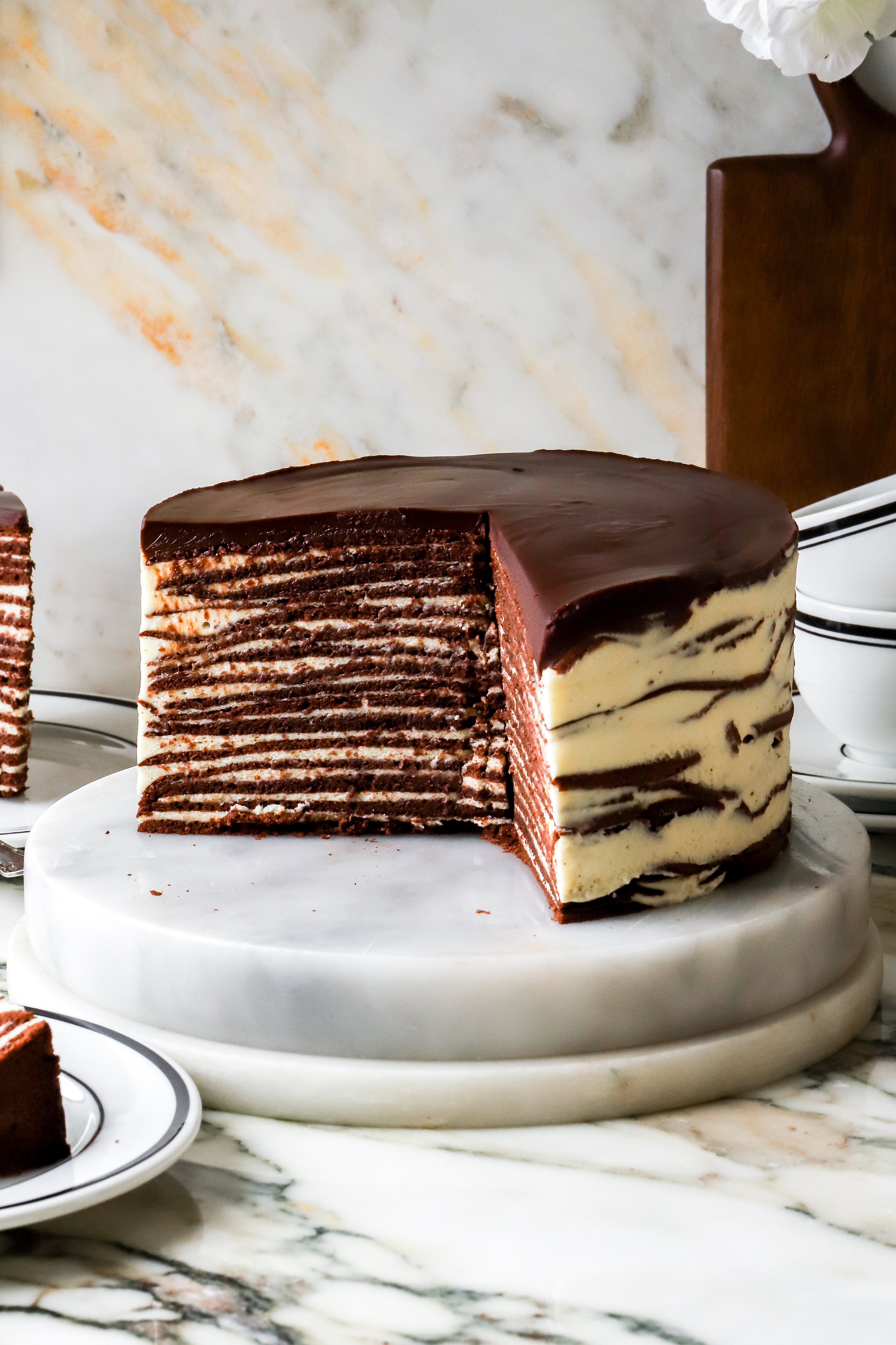 reverse dobos cake with chocolate cake layers and vanilla cream. cake sliced open on a marble countertop
