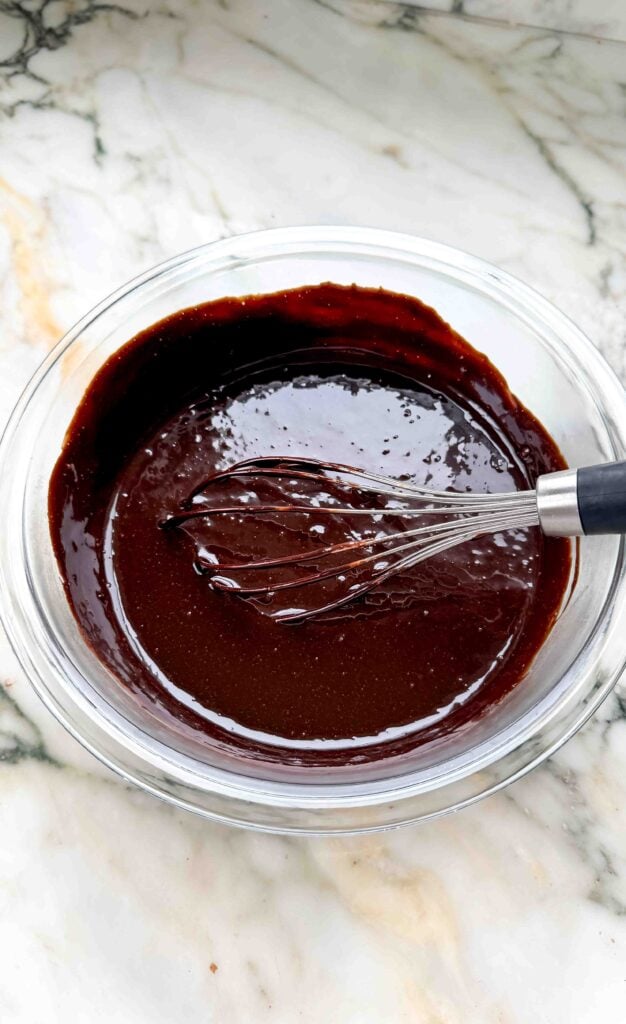 chocolate custard finished cooking in a glass bowl with a whisk