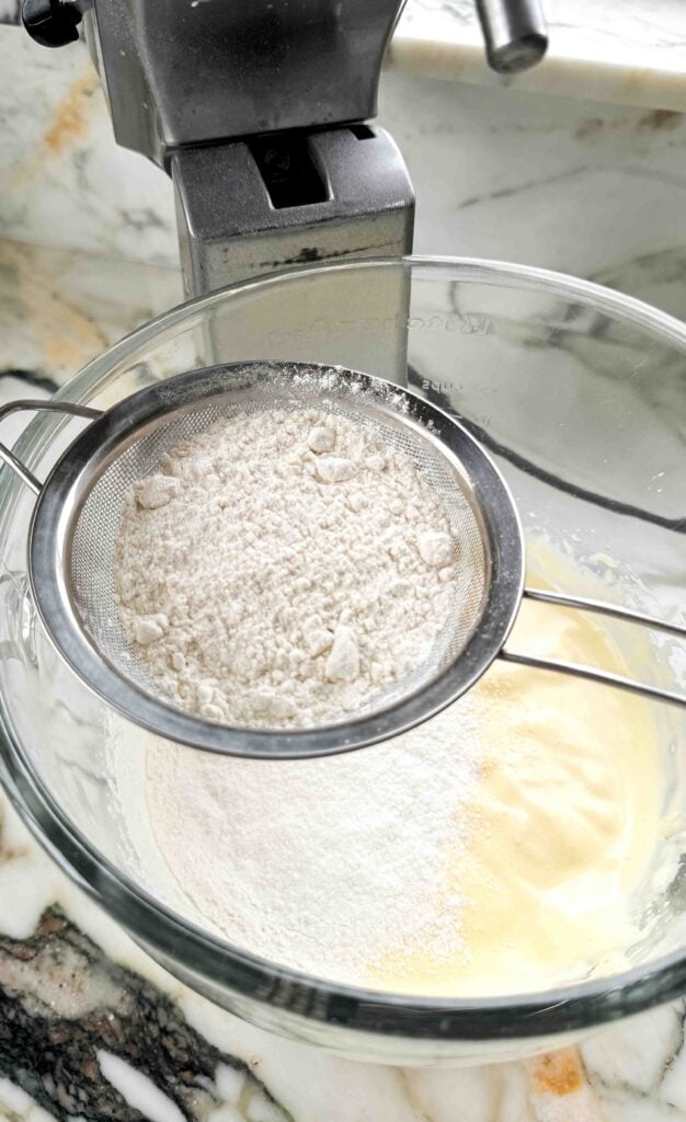 flour sifted on top of beaten egg yolks in the glass bowl of a stand mixer