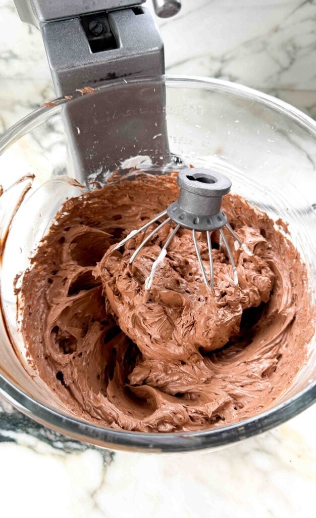 finished chocolate buttercream in the glass bowl of a stand mixer with the whisk attachment