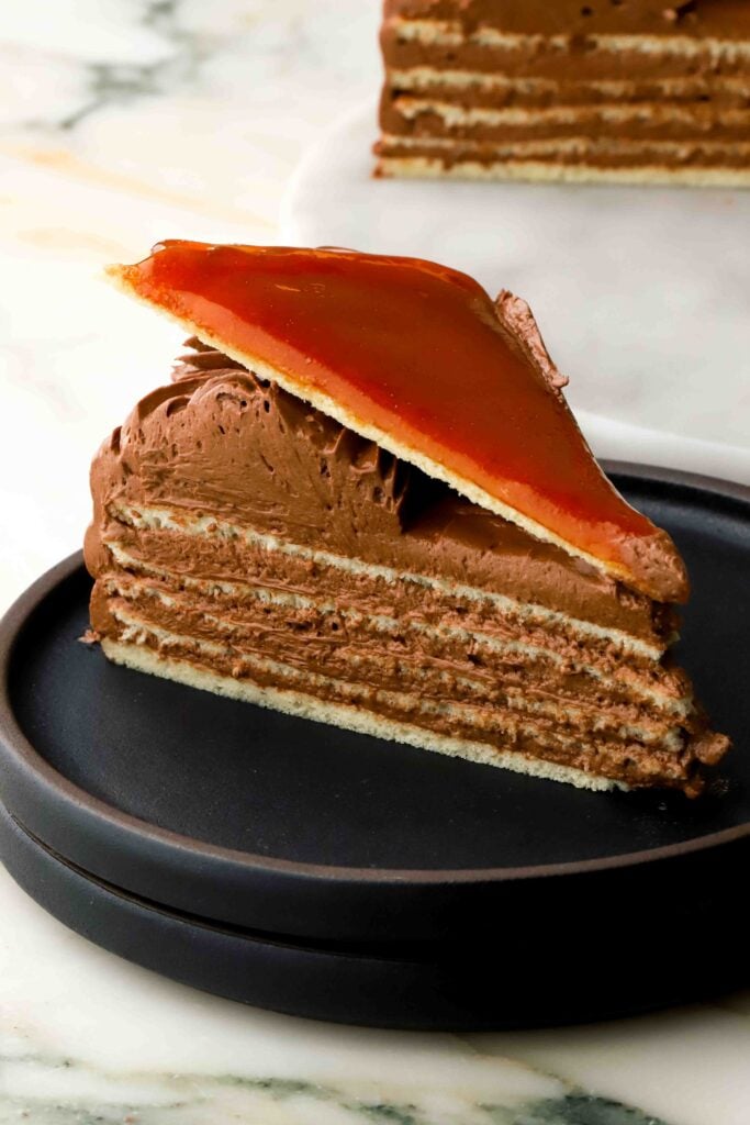 close up of a slice of authentic dobos on a plate with 5 layers of sponge, chocolate buttercream and a caramelized sugar triangle on top
