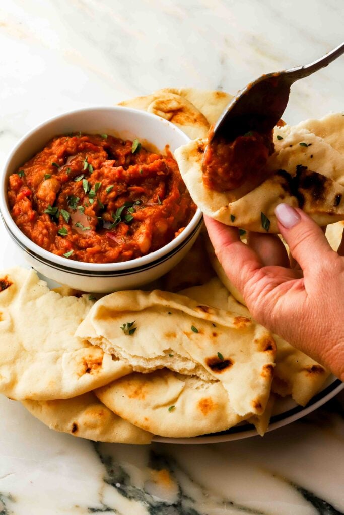 bowl of zacusca on a plate with naan bread, a spoon scooping some onto the bread