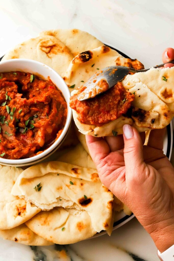 bowl of zacusca on a plate with naan bread, a spoon scooping some onto the bread