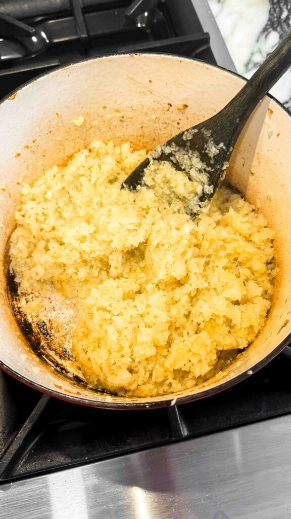 onions sauteed in oil in a dutch oven with a wooden spoon